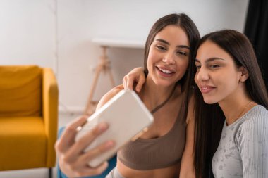 Genç bir kadının modern akıllı telefondan selfie çekmesine sevindim. En iyi arkadaşlar ya da kız kardeşler iç mekanda birlikte vakit geçiriyorlar.