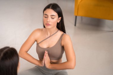 Huzurlu genç kadınlar kız kardeşiyle yoga yapıyor, yerde bacaklarıyla oturuyorlar. Meditasyon, rahatlama, bilinç temizleme konsepti. Gözler kapalı, dua işareti
