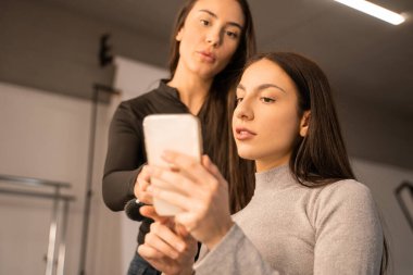 Stüdyodaki makyaj sanatçısına akıllı telefondan referans gösteren esmer kadın görüntüsü. Görünüm süreci kavramı