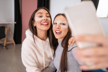 Göz bandı takmış iki komik kız kardeş evde cep telefonu kullanarak selfie çekiyor. Güzellik rutini ve arkadaşlık kavramı. Stok fotoğrafı