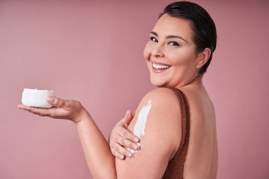 Günlük cilt bakımı. Duştan sonra vücut losyonu süren çıplak kadın portresi, pembe stüdyo arka planı, pankart, panorama, bedava fotokopi alanı