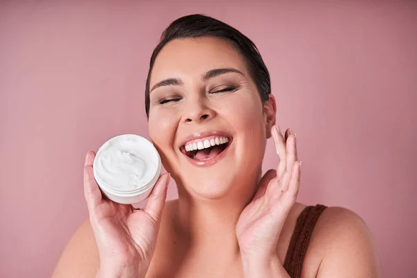 Happy woman excited about product for body against on pink studio background. Face of body positive model with smile for lotion or sunscreen for healthy glow. Cream and skincare concept