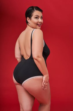 Kendini kabullenme, sevgi ve ilgi. Kırmızı stüdyo arka planında izole edilmiş kameraya bakan, mükemmel ciltli, yarım yamalak gülümseyen kadının portresi.