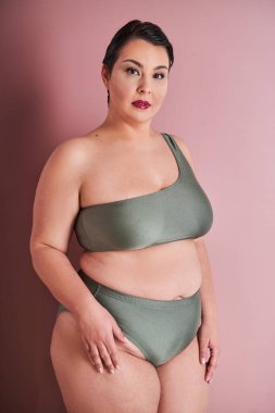 İç çamaşırlı yarı dönüşmüş bir kadının profil portresi pembe stüdyo arka planında kameraya bakıyor. İç çamaşırlı kadın pozu. Artı boyut modeli konsepti