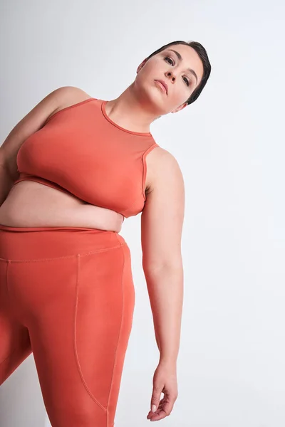 stock image Confident woman in sportswear looking at camera and posing over white studio wall. Healthy plus size female standing alone