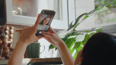 Akıllı telefonunu tutan ve evde selfie çekerken kameraya poz veren kadının görüntüsü. Teknoloji ve insanlar kavramı