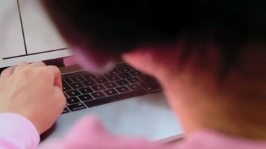 Evde ders çalışırken klavye çalan konsantre genç kız görüntüsü. Pembe kazaklı kadın ev işi yapıyor.