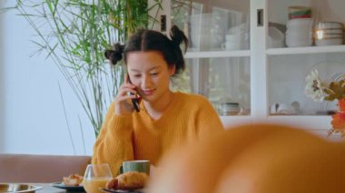 Oturup mutfakta kahvaltı ederken akıllı telefonun başında arkadaşıyla konuşan tatlı esmer bir kadın. Sabah konsepti