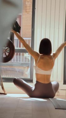 Yoga egzersizinden sonra dinlenerek yerde oturan sağlıklı genç bir kadının dikey görüntüsü. Güneşli sabah huzurlu atmosfer