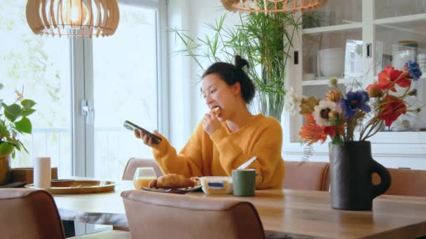 Concentrado Menina Asiática Comendo Enquanto Assiste Vídeo Interessante Seu Smartphone — Vídeo de Stock