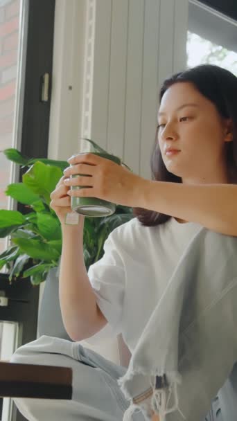 Asyalı Kadının Sıcak Çay Fincanı Alıp Pencerenin Yanındaki Apartmanında Otururken — Stok video