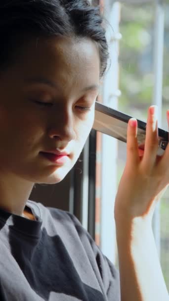 居心地の良い枕に座って友人からの声のメッセージを聞く本格的なアジアの少女の垂直ショット 国内のライフスタイルと技術コンセプト — ストック動画