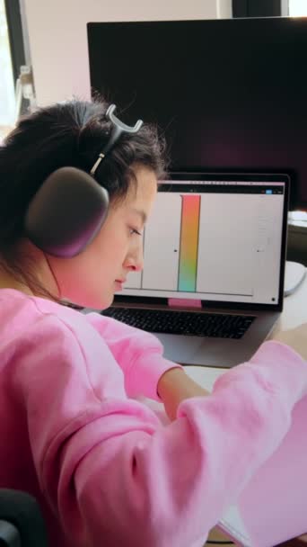ノートパソコンを持って家で勉強しながらノートを読んでいるアジアの女の子の垂直ショット かわいいですティーン読書宿題勉強リモート — ストック動画