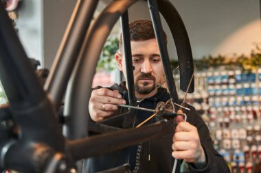 Ciddi bisiklet tamircisi, atölyede konuşan bir bisiklet tekeri kontrol ediyor. Bisiklet servisi, tamir ve geliştirme. Araç gereç ve ekipman ile garaj içi