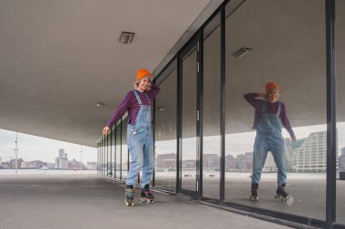 Modern şehir mekanında dengeyi sağlamak için paten sürmeyi öğrenen aktif funky kadının tüm vücut portresi.