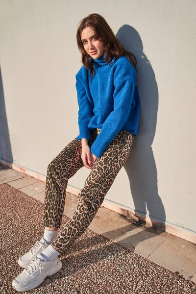 stock image Vertical view of the brunette woman in perfect and stylish look posing in relaxed pose to the camera while standing near the wall at sunny street