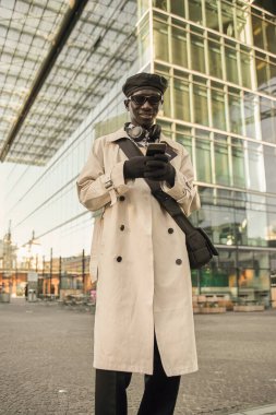 Havalı giysiler içinde gülümseyen koyu tenli bir adam sokakta dikilirken akıllı telefonlardan sohbet ediyor. Teknoloji ve insanlar kavramı
