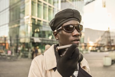 Moda kıyafetleri giyen çok ırklı bir adam cep telefonundan sesli mesaj kaydediyor. Teknoloji ve insanlar kavramı