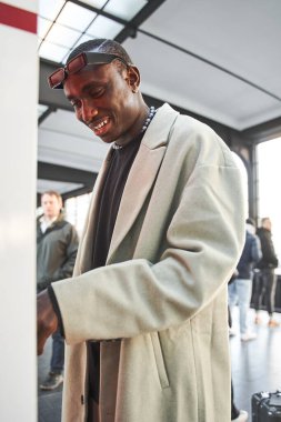 Neşeli, çok ırklı adamın tren istasyonunda dururken özel makineden bilet alışının dikey görüntüsü. Halk yaşam tarzı konsepti