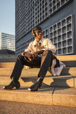 Kablosuz kulaklık takan bir adam güneşli cadde merdivenlerinde oturuyor ve gözünü kaçırıyor. Teknoloji ve insanlar kavramı