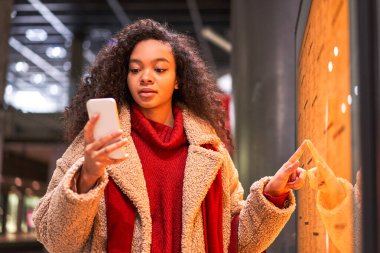 Metro haritasına parmağını tutarken cep telefonuna bakan sakin kıvırcık kadının belden yukarı portresi. Seyahat konsepti