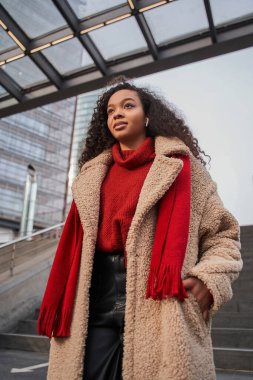 Çok ırklı kıvırcık kadının dikey görüntüsü uzaklığa bakıyor ve şehir yürüyüşünde müzik dinliyor. Halk yaşam tarzı konsepti