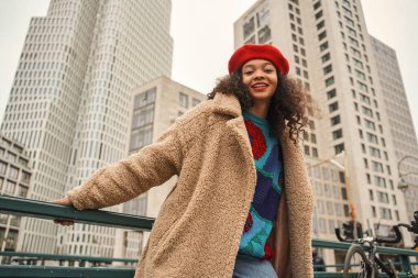 Zengin çok ırklı kadın kameraya bakıyor ve arka planda gökdelenlerle şehirde yürürken poz veriyor.