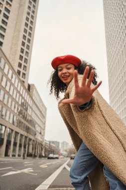 Kameraya elini uzatan ve dişlek bir gülümsemeyle poz veren kırmızı şapkalı zarif bir kadının dikey portresi. Halk konsepti