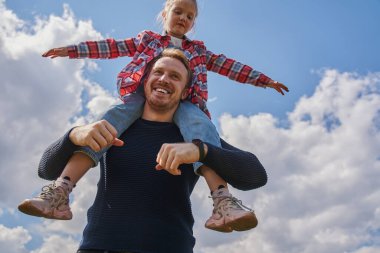 Yaz sokağında oynayan baba ve kız çocuklarının neşeli aileleri. Mavi arka planda kızını omuzlarında tutan mutlu bir adam.