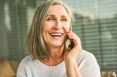 Rahat bir evde otururken mutlu yüzlü akıllı telefondan konuşan aşırı neşeli bir kadın. İnsanlar ve teknoloji kavramı