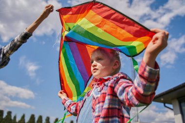 Gökkuşağı uçurtması tutan küçük bir kız ve ailesiyle temiz havada oynarken mesafeye bakıyor. Halk yaşam tarzı konsepti