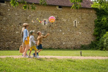 Çocuklar anne ve büyükbabalarıyla yürürken çimlerin üzerinde renkli uçurtmalarla oynuyorlar. Mutlu çocukluk anları ya da açık hava zaman harcama kavramı