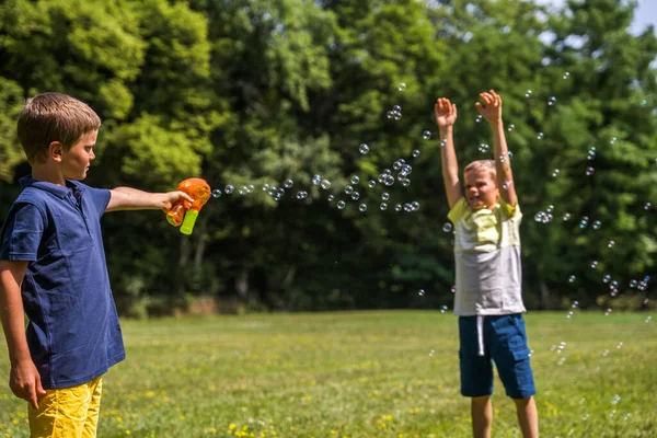 Happy boys summer game. Kids playing, shooting with soap bubbles during hot weather. Little brothers street games. Summertime joy activity and recreation concept