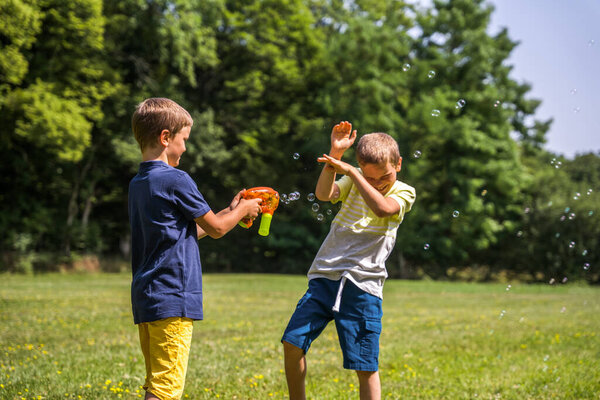 Два милых брата делают друг другу мыльные пузыри в городском парке. Дети играют в жаркую погоду. Концепция летних развлечений
