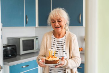 Yaşlı bir kadın sevinçle yanan mumlarla kutlama pastası getirir..