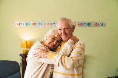 Mutlu yaşlılar doğum günü kutlaması için birbirlerine sarılıyorlar. Evde yaşlılar için uzun yaşam kavramı. Birlikte kameraya bakıyoruz..