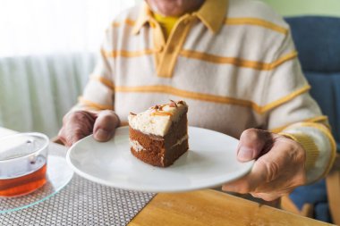 Bir masanın arka planında elinde pasta olan yaşlı bir adamın yakın plan fotoğrafı..