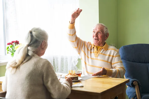 An elderly couple sitting at home at the table, conversing, morning routine at home. Concept of happy aging together.