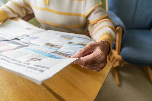 Close up of old hands pensioner reading fresh press at home, domestic routine. Concept of centenarians.