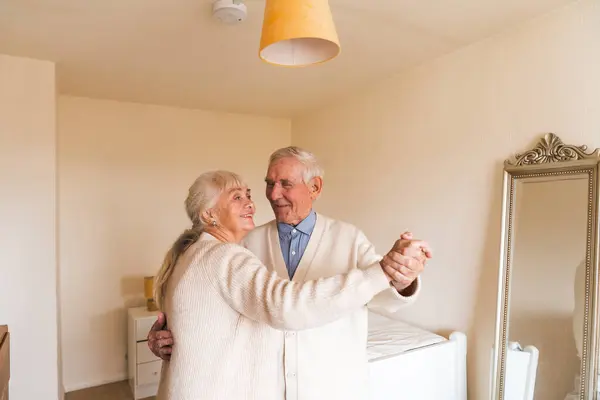 An elderly couple dancing together in their well-lit room, happy years together. Concept of aging.