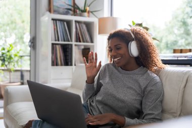 Kulaklık takan Afro-Amerikan bayan, laptoptaki video konuşmasında arkadaşıyla konuşuyor. Teknoloji ve insanlar kavramı