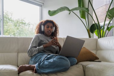 Kulaklık takan Afro-Amerikan bayan, laptoptaki video konuşmasında arkadaşıyla konuşuyor. Teknoloji ve insanlar kavramı