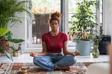Nefes al ve rahatla. Huzurlu genç bir kadının evde meditasyondan zevk aldığının portresi. Gözleri zevkten kapalı.