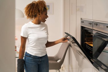 Gülümseyen Afrikalı Amerikalı kadın sobanın yanında duruyor ve mutfakta yemek pişiriyor. Fırın konsepti. Stok fotoğrafı