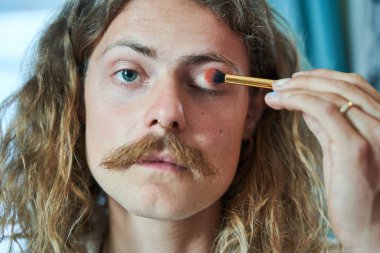 Bıyıklı, göz farı sürerek iç mekandaki duvarlara bakan modaya uygun gey adamın portresi. İnsanların güzellik konsepti