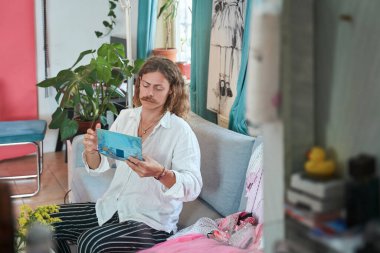 Bıyıklı, el ele tutuşan ve ciddi bir yüz ifadesiyle kanepeye bakan metroseksüel bir adam. İnsanların güzellik konsepti