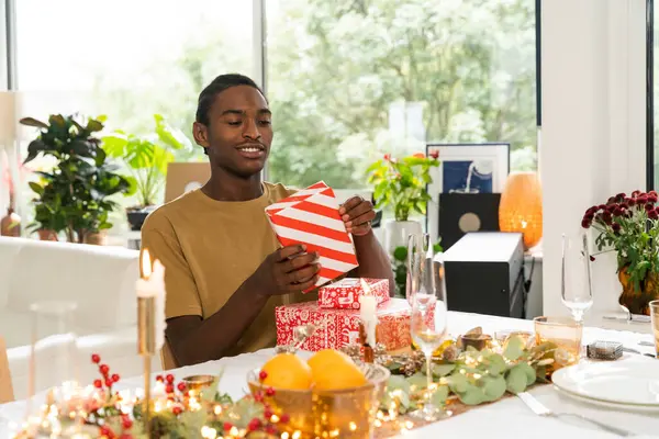 Happy african american man recieving gift from loving woman while sitting at the New Year table. People and holidays concept