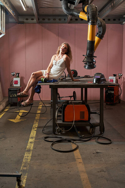 Attractive womanlike carpenter in female dress sitting at the table and posing at his workplace. Occupation concept