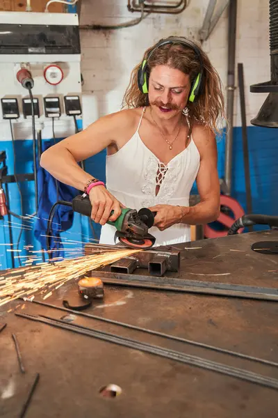 Happy lumber craftsman working with his equipment in workshop. Smiling longhaired feminine guy enjoying his work