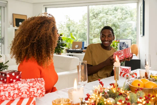 Счастливый Африканский Американец Получает Подарок Любящей Женщины Сидя Новогодним Столом Лицензионные Стоковые Фото